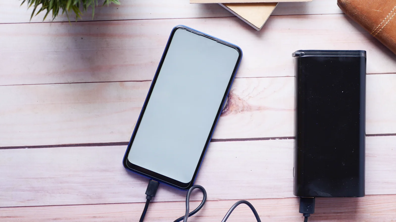 Telefon podłączony przewodem do neutralnego powerbanku na drewnianym blacie